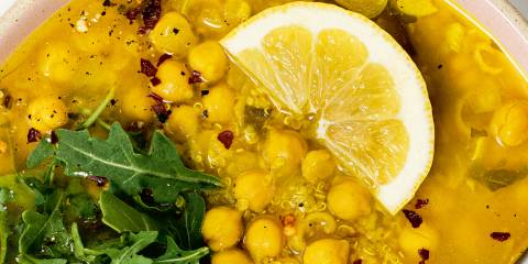 a bowl of chickpea soup garnished with arugula and lemon
