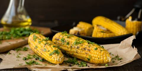 Grilled Lime & Cilantro Corn on the Cob on parchment paper with corn, oil and cilantro in the background.