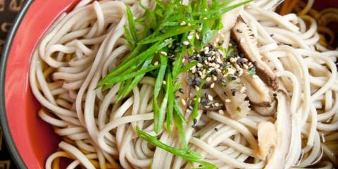 a bowl of soba noodles garnished with sesame seeds and scallions
