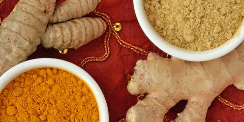 Powder and roots of turmeric and ginger on indian carpet background