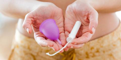 a woman holding a menstrual cup and a tampon