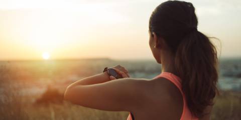 Woman checking workout goals on smart watch looking towards the sunset.
