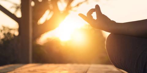 View of a woman's knee and hand in yoga pose, sunset in the background.