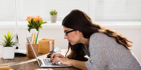 A woman on her computer hunched over working.