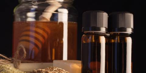 A jar of honey with essential oil bottle against a black background.