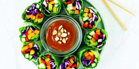 Colorful veggies wrapped in lettuce, positioned vertically around a dish of hoisin sauce.