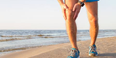A man with an aching knee while running on the beach