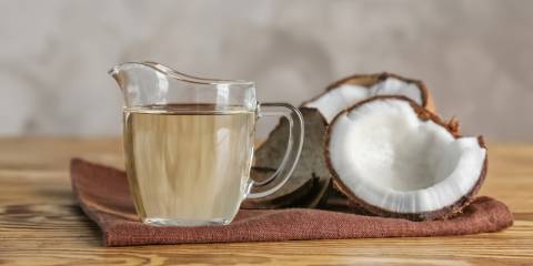 Ripe coconut and pitcher with MCT oil on a wooden table.
