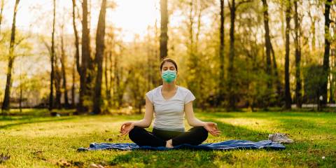 a woman wearing a mask, meditating in a sunny park