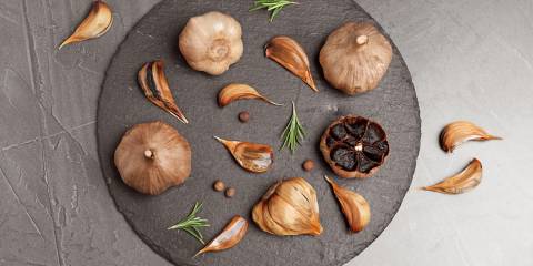 Slate plate with aged black garlic and rosemary on gray background, top view.