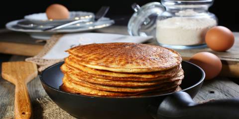 Stack of pancakes on a plate with eggs and flour in the background