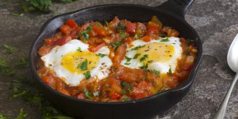 two eggs nestled in chopped tomatoes and red bell peppers in black skillet