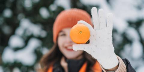a healthy woman outdoors in winter holding up an orange