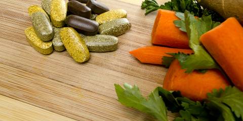 Vitamins next to some vegetables on a wooden table. 