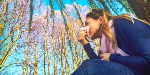 A woman under a willow tree wiping her nose with a tissue.