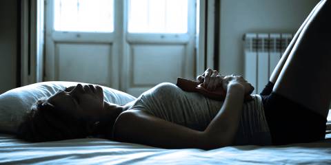 A woman laying down in the dark with a hot water bottle on her abdomen