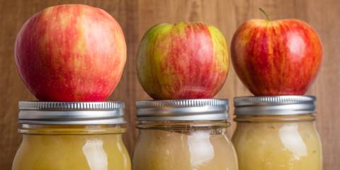 Three apples on top of mason jars filled with apple sauce 