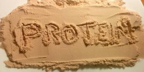 The word protein written in a layer of beige protein powder.