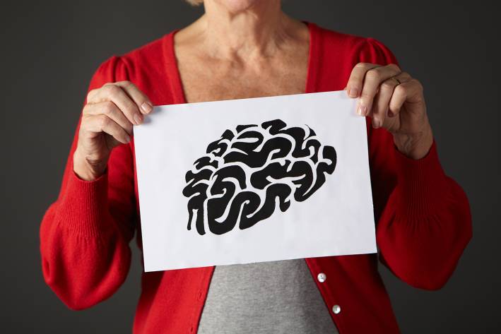 An older woman holding up an illustration of a brain