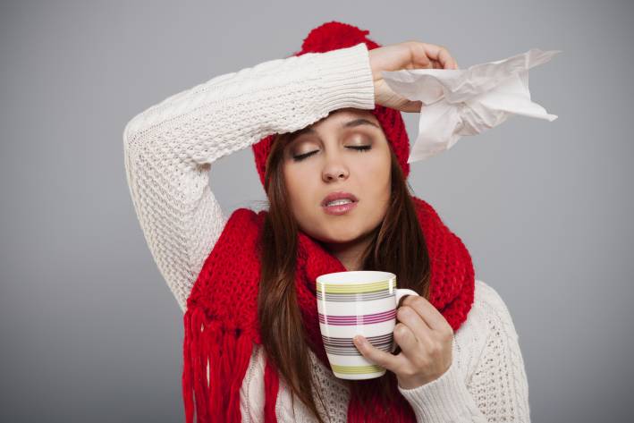 Surviving Cold and Flu Season woman in a hat and scarf with a tissue in her hand drinking tea