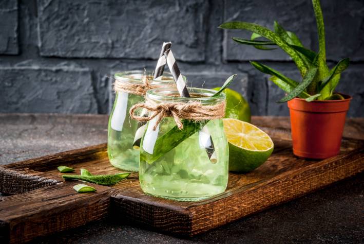 Aloe infused Lime water in drinking jars with black and white paper straws on a cutting board.