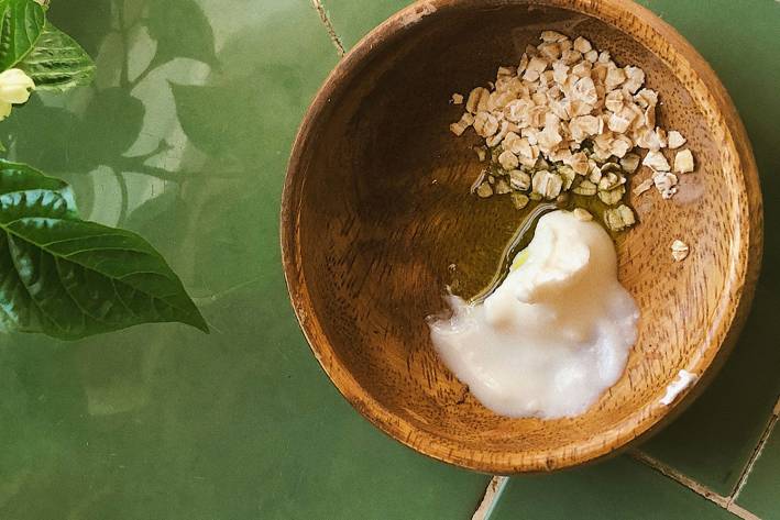 A top view of wooden bowl with oats, oil and yogurt on a green tile countertop.
