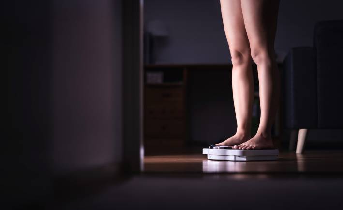A view of a woman's legs standing on a scale in a dark room.