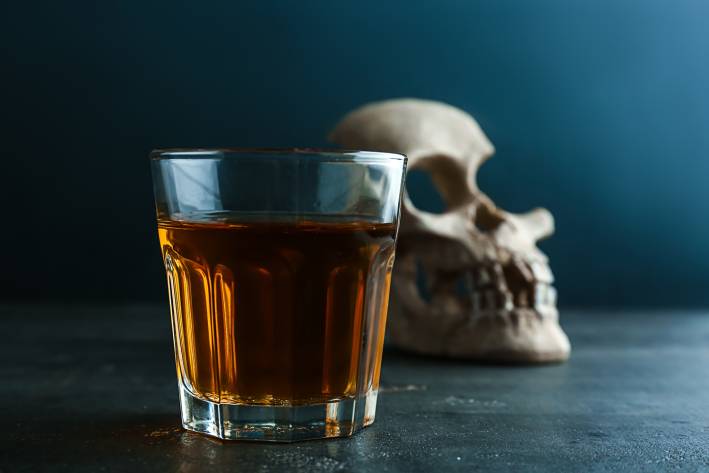 Glass of whiskey with skull on table