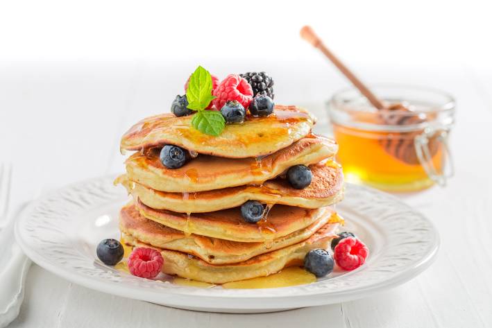 a stack of fluffy pancakes with berries and honey