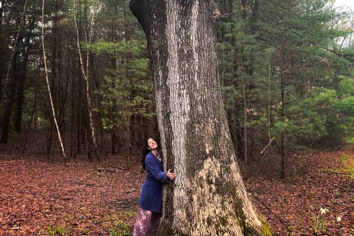 Amy hugging a very tall tree at the edge of the woods