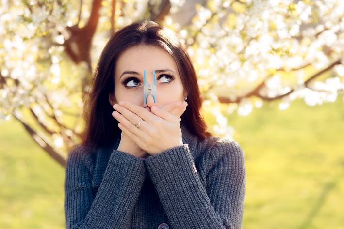 a woman outside sneezing with a clothespin on her nose
