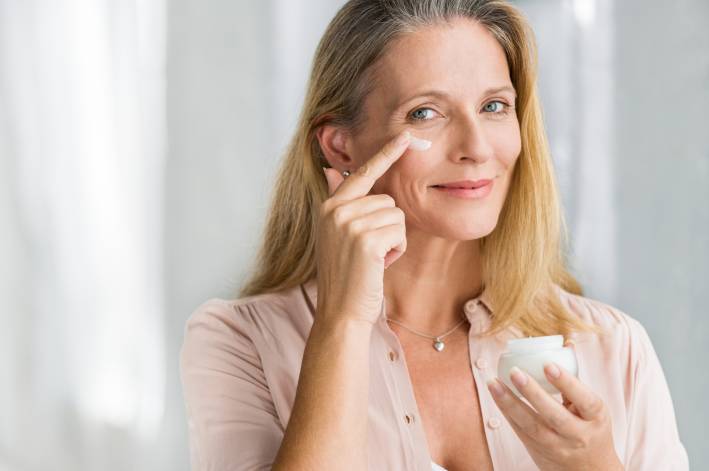 Woman applying anti-aging cream on her face. 