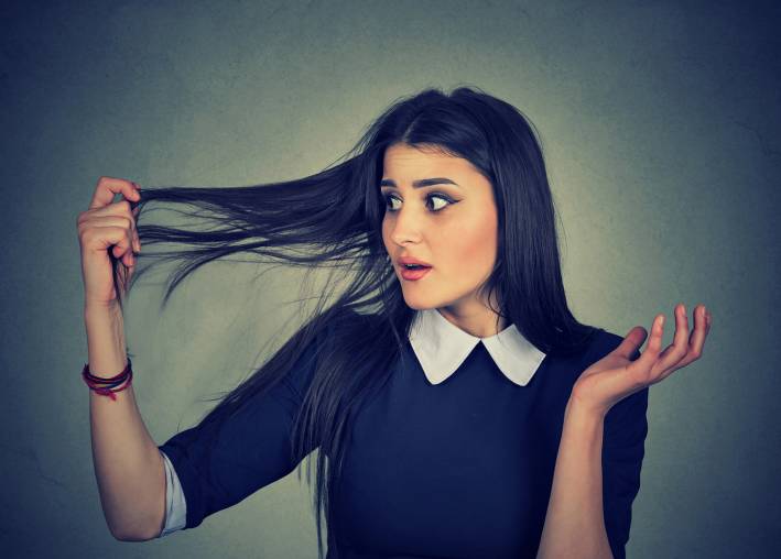 A surprised young woman holding her thinning hair