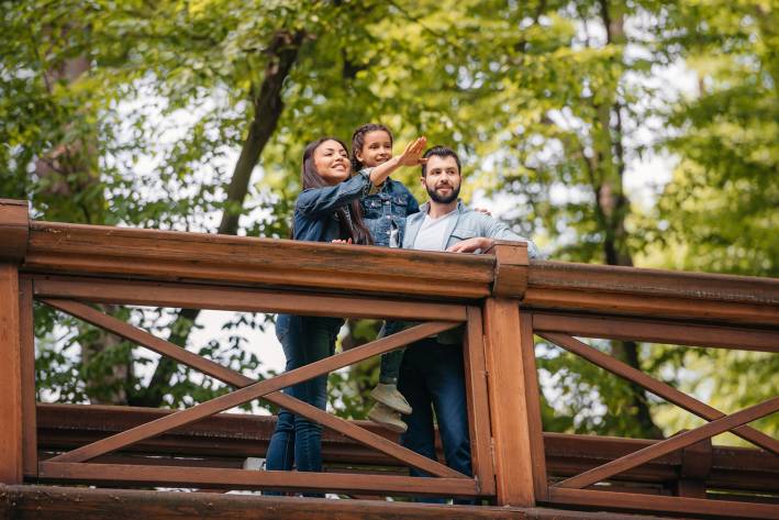 Happy interracial family standing on wooden bridge, while mother pointing somewhere