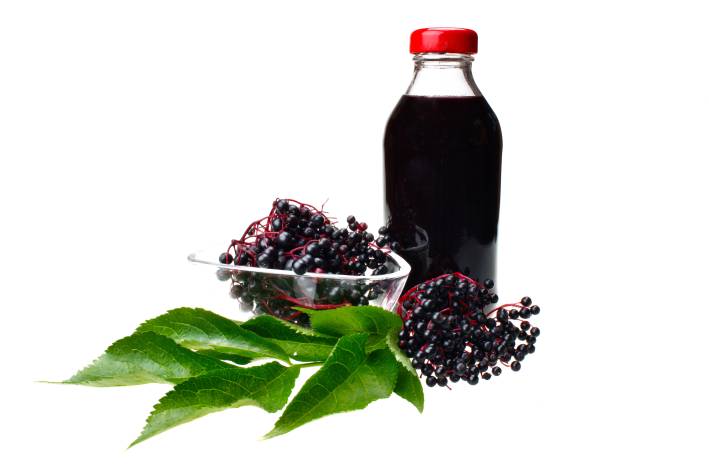 A glass jar of elderberry juice beside elderberry fruit bunches.