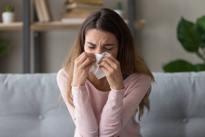 a sick woman sneezing into a tissue