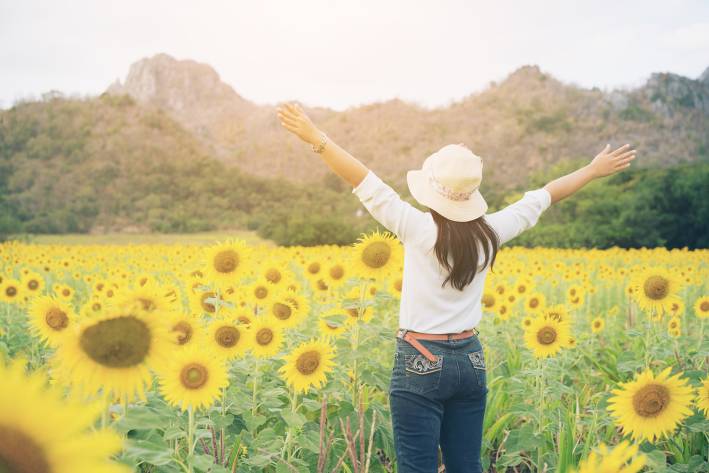 Woman in sunflower field with arms raised to the sunshine.