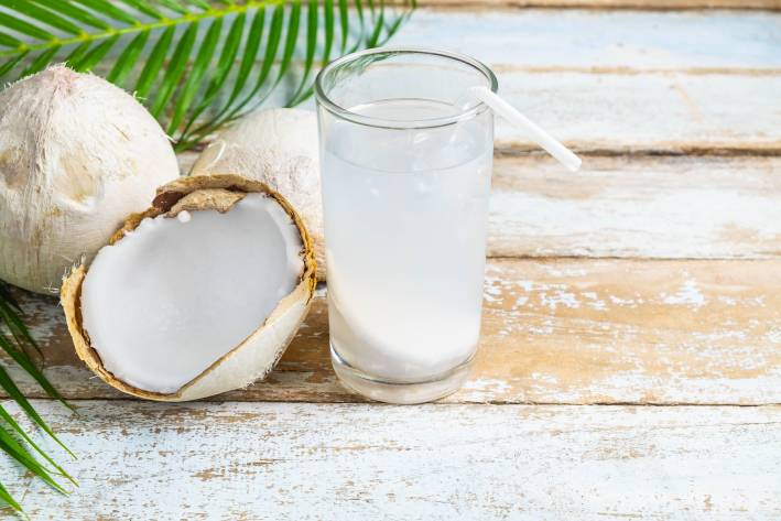 A glass with coconut water next to a coconut split in half. 