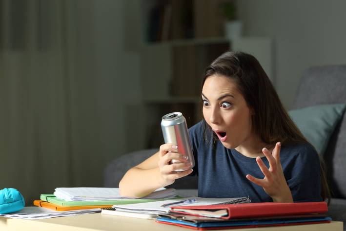 a young woman studying, looking at her energy drink can in surprise