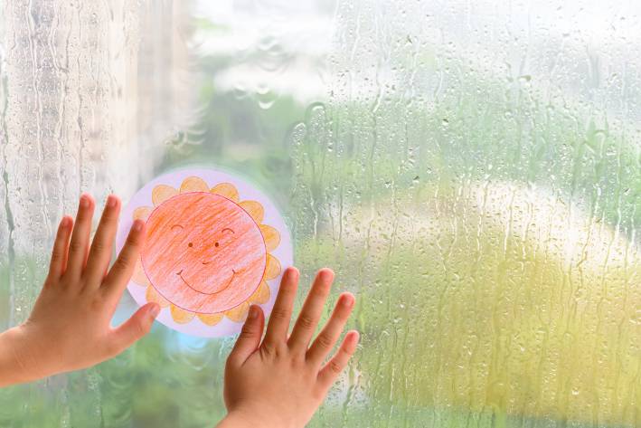 a child holding a paper sun up to a window on a rainy day