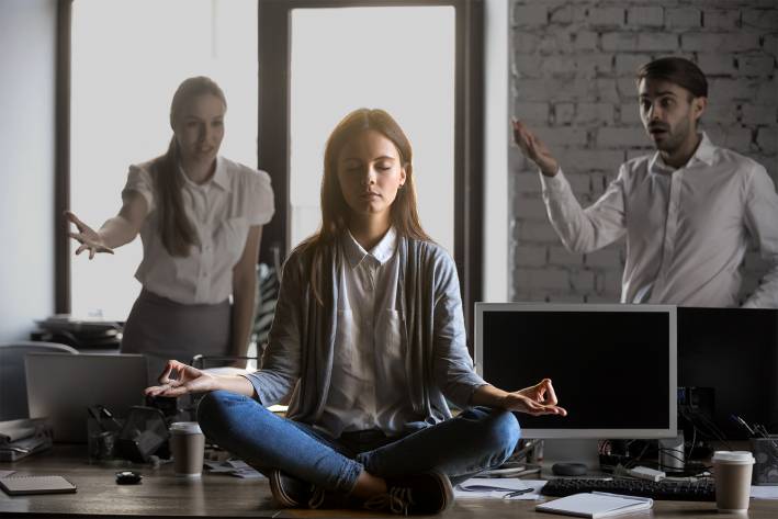a woman meditating in an office with stressful coworkers