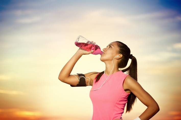 an athletic woman drinking a cherry-flavored supplement drink