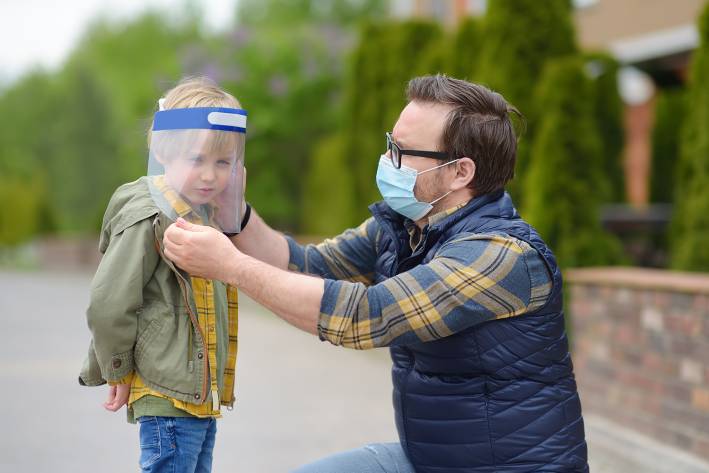 a masked man putting a face shield on his son