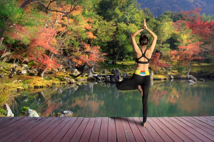 Find Your Balance with Tree Pose Woman in work out clothes doing tree pose on the dock of a pond during fall.