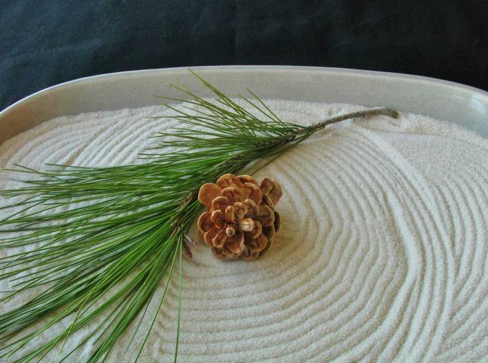 A personal zen garden with a sprig of pine and a pine cone on it.