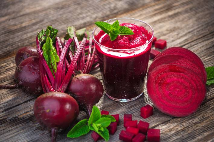 A glass of beet juice accompanied by fresh beets on a rustic picnic table. 