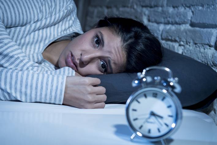 Woman awake in bed with clock in view.