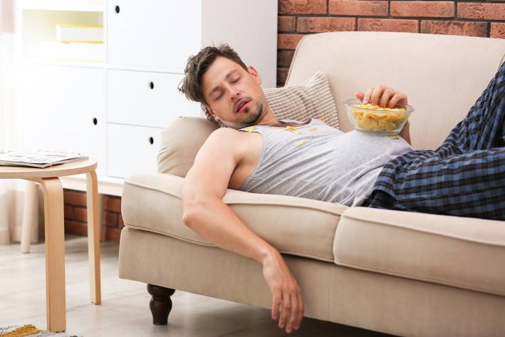 a man that fell asleep on the couch eating junk food