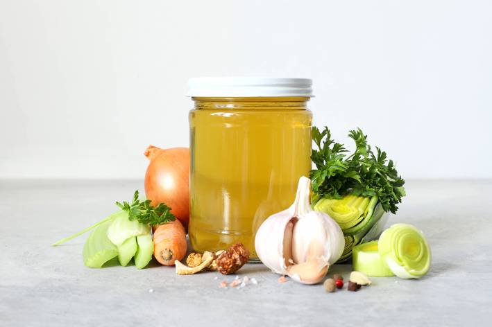 a jar of broth and some prepped vegetables