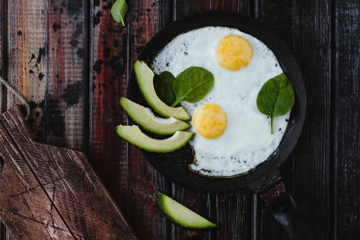 Fried eggs in a cast iron pan, with avocado slices garnished with spinach.